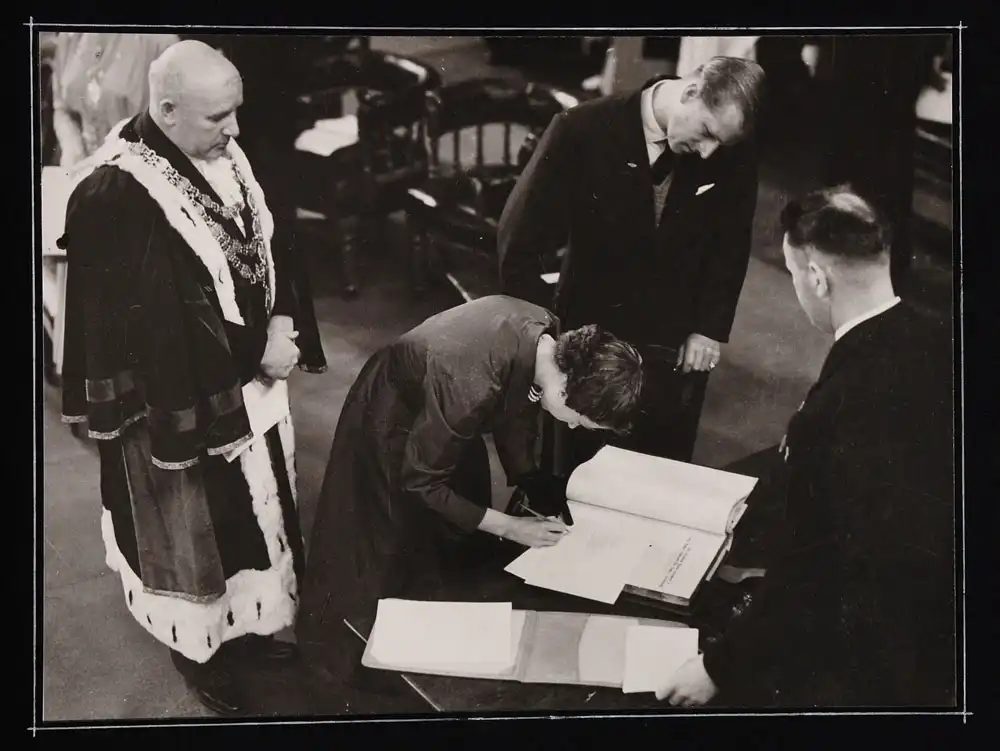Photograph reproduction. Queen Elizabeth II signing the Dunedin Public Library visitor’s book, with the Duke of Edinburgh standing to her left, 26 January 1954.  - Courtesy of the Dunedin City Council Archives.