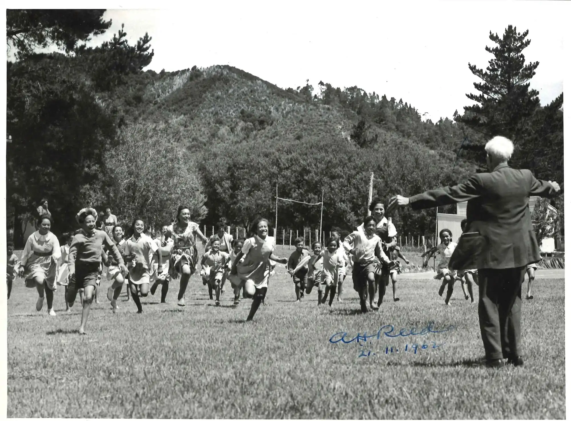 Photograph of children running towards A.H. Reed at an unidentified North Island school, 1962. Photograph by Tudor Collins.